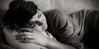 person lying down with hands around pillow under head